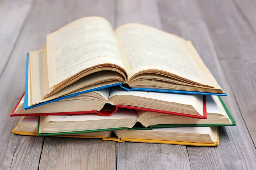 Four open books in the colored cover on the table made of boards.A stack of books in the colored covers on the table with a red tablecloth. Still life with books.